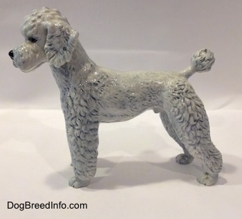 The left side of a porcelain white with blue Poodle figurine. The figurine ears are flopped over.