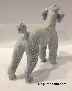 The back right side of a figurine of a porcelain white with blue Poodle. The figurine has a short poofy tail.