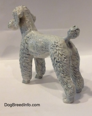 The back left side of a porcelain white with blue porcelain Poodle. The ears of the figurine are detached from the head of the figurine.