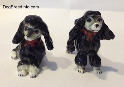 Two black with white bone china Poodle figurines. One figurine is lying down and the other is standing.