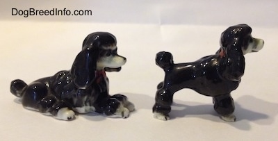 The right side of two black with white bone china figurines of Poodles. Both figurines have short hair poofy tails.