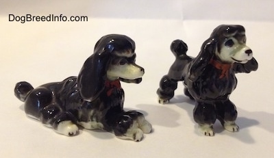 The front right side of two bone china figurines of black with white Poodles. The figurines are wearing red bowtie collars.