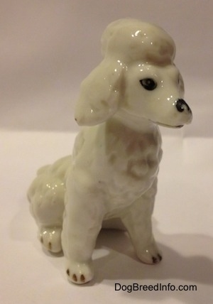 A white bone china Poodle figurine that is in a sitting position. The figurine has black tipped nails.