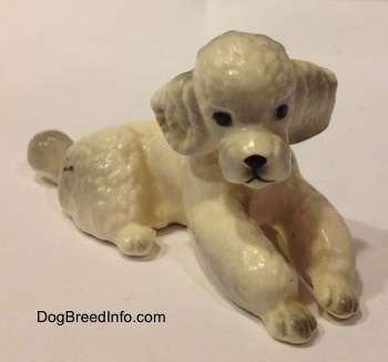 A white ceramic Poodle figurine that is in a lying position. The figurine has black circles for eyes.