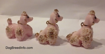 The right side of three figurines of a pink spaghetti Poodle puppy. Two of the figurines are in a sitting position.