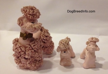 A pink spaghetti porcelain Poodle set of figurines. There are three figurines of a Poodle, one adult and two puppies.