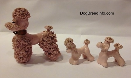 The left side of three pink spaghetti porcelain Poodle figurines. The adult figurine has on agold collar.