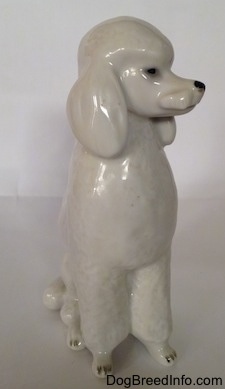A porcelain figurine of a white standard Poodle in a sitting pose. The figurine has a poof of hair at the top of its head.