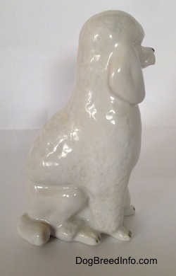 The right side of a white porcelain standard Poodle in a sitting pose figurine. The figurine has a tail along the side of its legs.