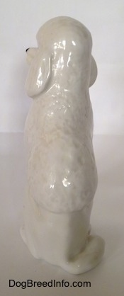 The back of a white porcelain standard Poodle figurine that is in a sitting pose. The figurine is glossy.