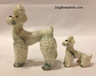 The left side of two Poodle figurines that are white with spots of gray. The Poodle puppy figurine is in a sitting position.