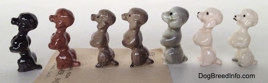 The left side of a Poodle puppy figurine in a begging pose with seven different color variations. The figurines have black circles for eyes.