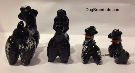 The back of four black clay figurines of Poodles. The figurines have short tails that are arched in the air.