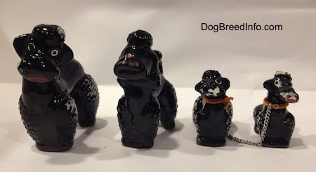 Four black clay Poodle figurines. Two of the figurines are adult and two are adults. Each figurine has a poof of hair on therehead.