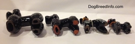 The underside of four figurines of black clay Poodles.