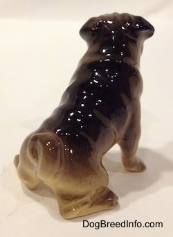 The back right side of a brown with black miniature Pug seated figurine. The figurine is glossy.