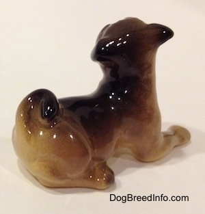 The back right side of a brown with black miniature figurine of a Pug lying down. The figurine has black ears.