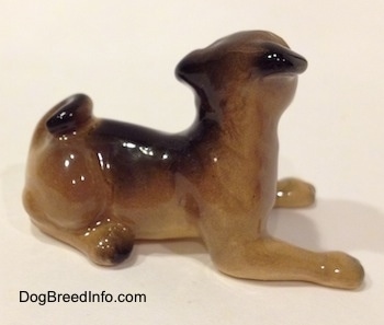 The right sid eof a brown with black miniature Pug figurine lying down. The figurine has short legs.