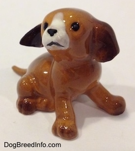 The front right side of a miniature puppy sitting figurine. The figurine is glossy.