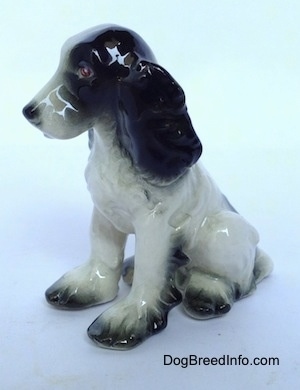 The front left side of a Russian Spaniel sitting figurine. The ears of the figurine are bumpy and black.