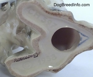 Close up - The underside of a white with black Russian Spaniel dog figurine. The figurine has a hole in the bottom of it. To the left of the hole is a black stamp the reads 'Germany'.