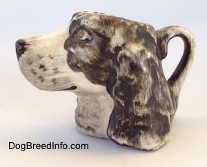 The left side of a stein cup that is of a brown and white Russian Spaniel dog. The handle of the stein is painted like the ears of the figurine.