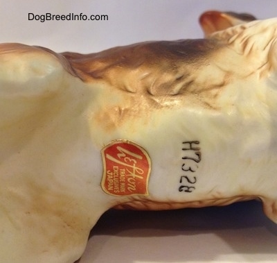 The underside of a porcelain Saint Bernard figurine that has a Lefton Co. sticker on it. and above that is the number 'H 7328'.