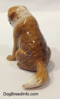 The back left side of a brown with white Saint Bernard sitting figurine. The figurine is glossy.