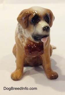 A brown with white figurine of a Saint Bernard in a sitting position figurine. The figurine has its mouth open and tongue out.