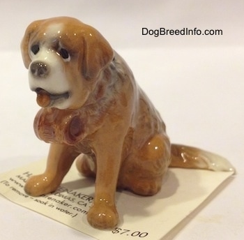 The front left side of a brown with white Saint Bernard miniature figurine that has a barrel on as a collar.