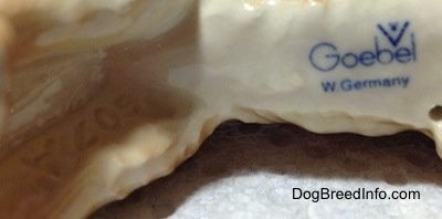 Close up - The underside of a figurine of a white with brown Saint Bernard figurine. There is the blue logo stamp of Goebel W.Germany.