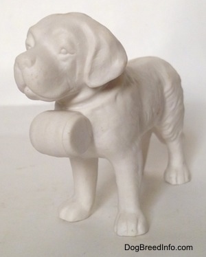 The front left side of a porcelain white bisque Saint Bernard figurine. The figurine has a barrel on its collar.