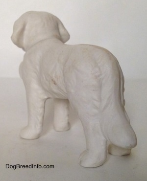 The back left side of a porcelain figurine of a white bisque Saint Bernard. The legs of the figurine are long.