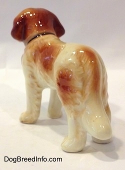 The back left side of a white with brown Saint Bernard figurine. The figurine has a long tail that is hard to differentiate from the body at the back left angle.