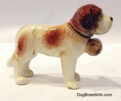 The right side of a figurine of a white with brown porcelain Saint Bernard figurine. The figurine has medium length white legs.
