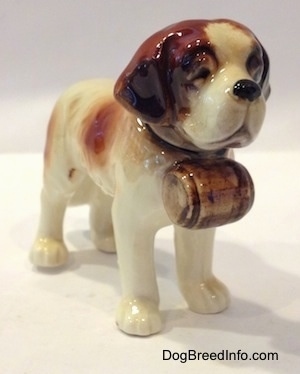The front right side of a white with brown porcelain Saint Bernard figurine. The figurine has a barrel under its head.