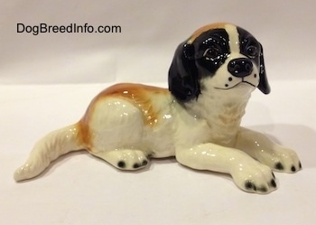 The right side of a figurine of a white and brown with black Saint Bernard puppy figurine. The face of the figurine is black with a white strip going down the middle and around its muzzle.