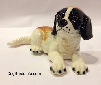 A white and brown with black figurine of a Saint Bernard laying down. The figurine has black tipped nails.