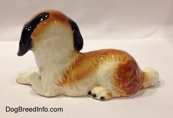 The back of a white and brown with black Saint Bernard puppy in laying down pose figurine. The figurine has fine hair details.