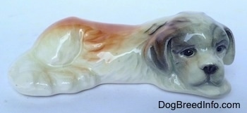 The right side of a white with brown and black Saint Bernard puppy in a lying position figurine. The figurine if glossy.