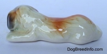 The left side of a Saint Bernard puppy figurine in a lying position. The figurine has a large brown spot across its back.