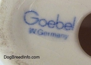 Close up - The underside of a white with brown and black Saint Bernard puppy figurine. The blue stamp of Goebel W.Germany is on the underside of the figurine.