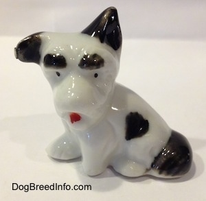 A white and black figurine of a bone china Schnauzer in a sittin pose. The figurine has black circles for eyes and a red tongue.