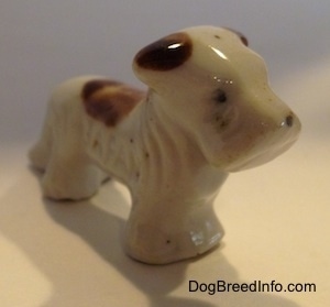 The front right side of a bone china white with brown Schnauzer figurine. The legs of the figurine are attached.