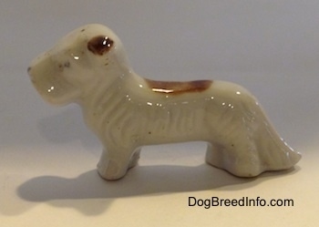 The left side of a figurine of a white with brown bone china Schnauzer. The ears of the figurine is brown.