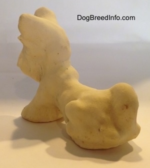 The back left side of a clay Miniature Schnauzer sitting figurine. The figurine has light hair details.
