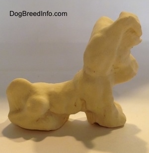 The right side of a clay figurine of a Miniature Schnauzer sitting. The figurine has short legs.