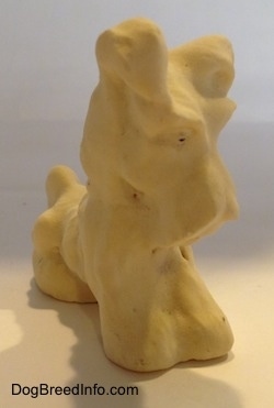 A clay figurine of a Miniature Schnauzer sitting. The figurine has small holes in the middle of its eyes.