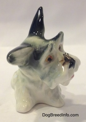 A figurine of a white with black miniature Schnauzer figurine in a sitting position. There is a fly on its nose.