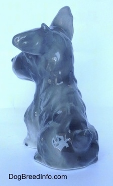 The back left side of a grey and white figurine of a miniature Schnauzer sitting. The figurines tail is hard to see at this angle.